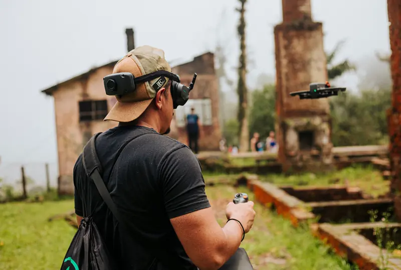 A man uses a drone in a misty, abandoned building site surrounded by greenery