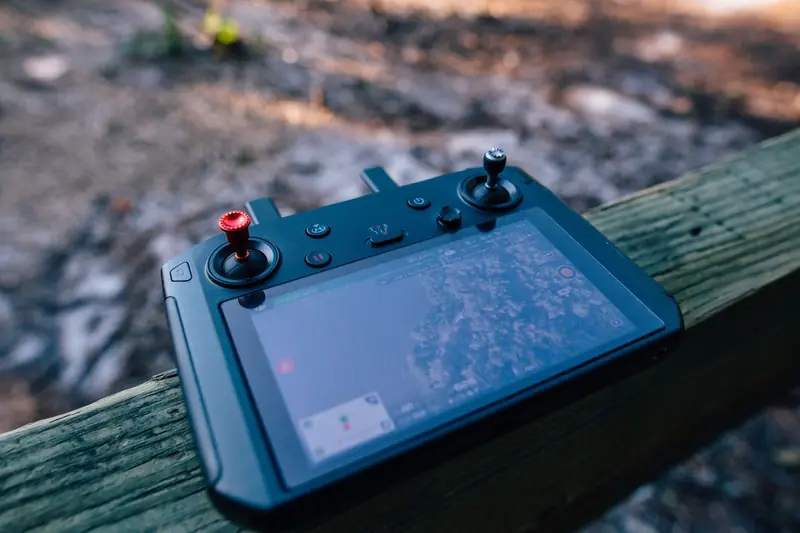 Close-up of a drone controller with visible screen, resting on a wooden surface outdoors