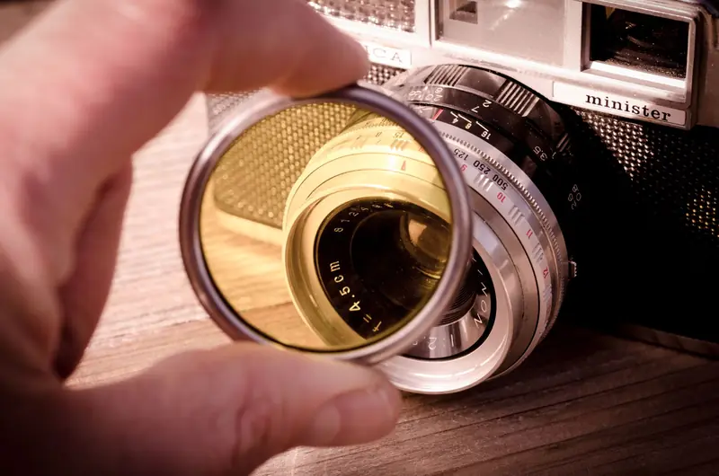 Close-up shot of a vintage camera with a yellow filter held in front of the lens