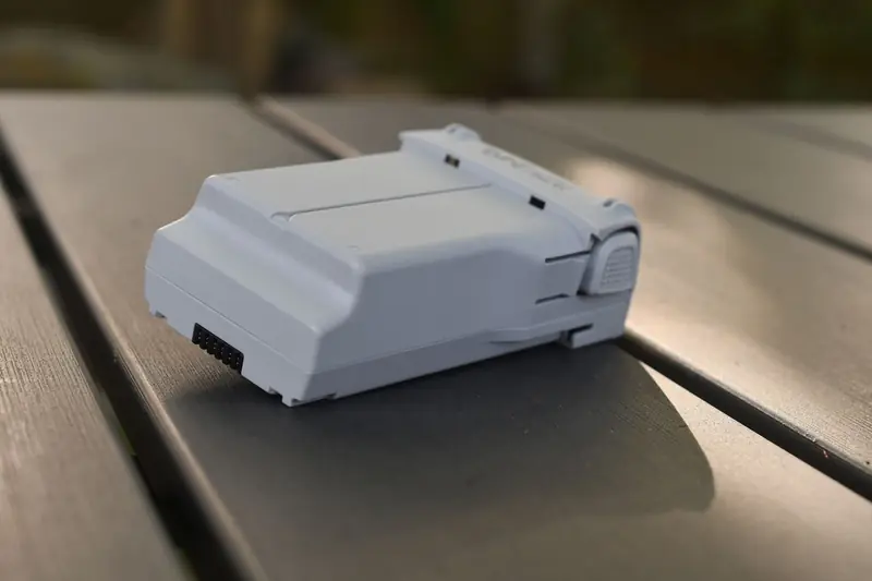Close-up of a modern drone battery placed on a wooden table outdoors, showcasing its sleek design