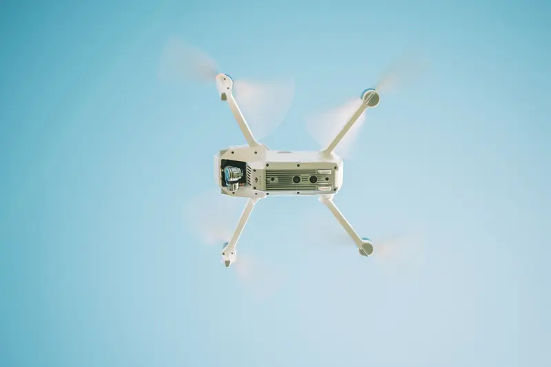 A sleek white drone flying under a clear blue sky, capturing aerial views