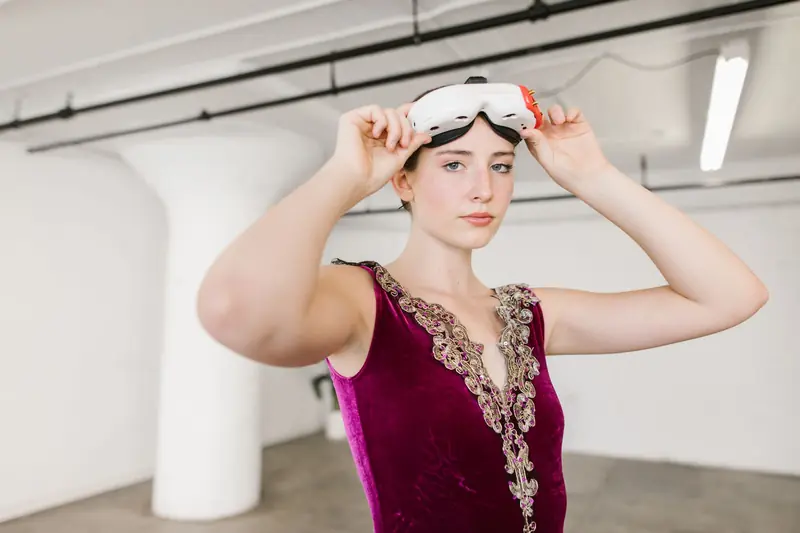 A woman adjusts virtual reality goggles while wearing an ornate dance leotard indoors