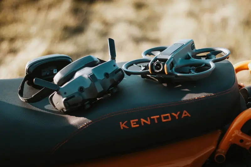 FPV drone and goggles placed on a motorcycle seat with 'Kentoya' visible, showcasing outdoor tech setup