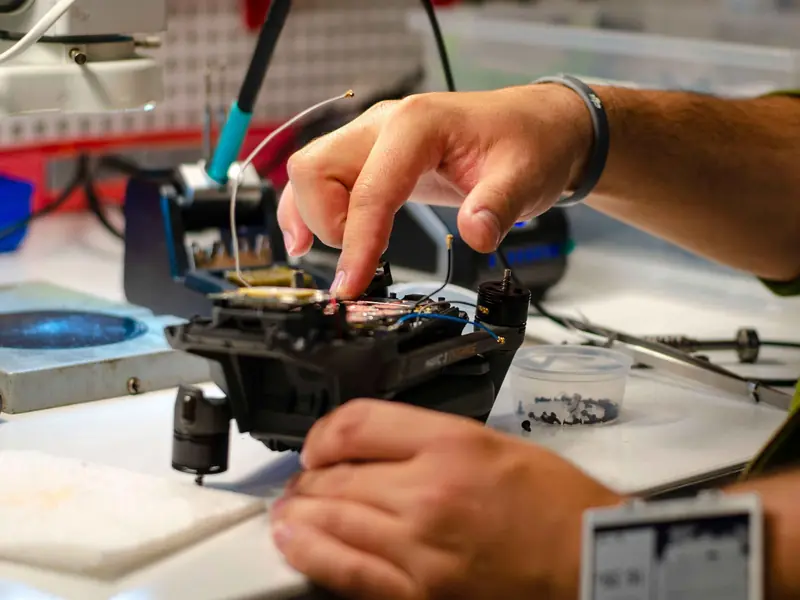 Hands of a technician performing drone repair on a workbench indoors