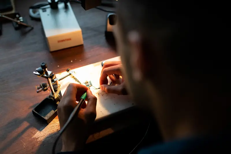 A focused engineer soldering a circuit board under bright light in a workshop setting